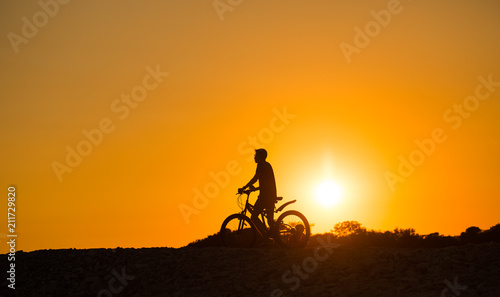 велосипедист с велосипедом стоит на закате 
