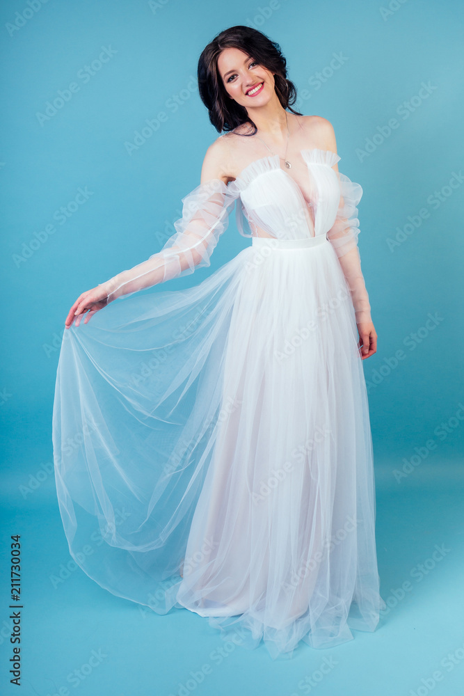 young and beautiful woman bride with makeup in long chic white wedding dress dancing ballroom waltz dance in studio on a blue background