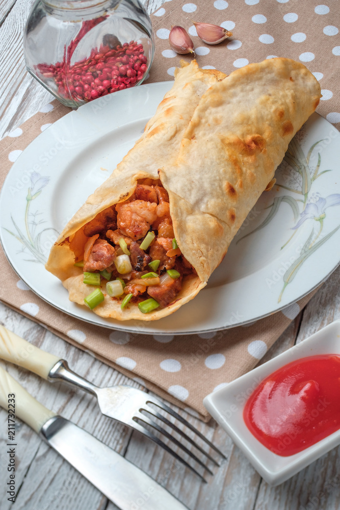 Doner kebab is lying on a white plate. Shawarma with meat, onions, salad lies on a white old wooden table. Doner kebab is lying on a white plate. Shawarma with meat, onions, salad lies on a white old wooden table.
