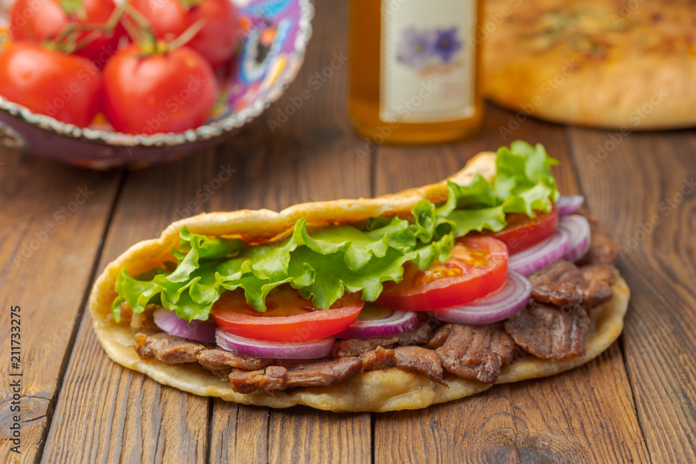 Delicious fresh homemade sandwich with chicken burspit roasted meat, tomato, onions and lettuce on wooden board on dark wooden table. Doner kebab. Healthy food concept. Delicious fresh homemade sandwich with chicken burspit roasted meat, tomato, onions and lettuce on wooden board on dark wooden table. Doner kebab. Healthy food concept.