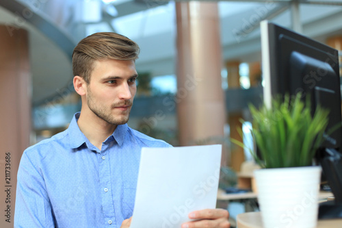 Young businessman reading paperwork at desk in office.