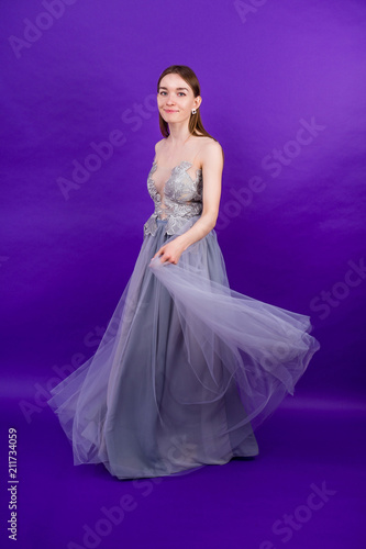 young and beautiful woman bride with makeup in long chic dress dancing ballroom waltz dance in studio on a purple background
