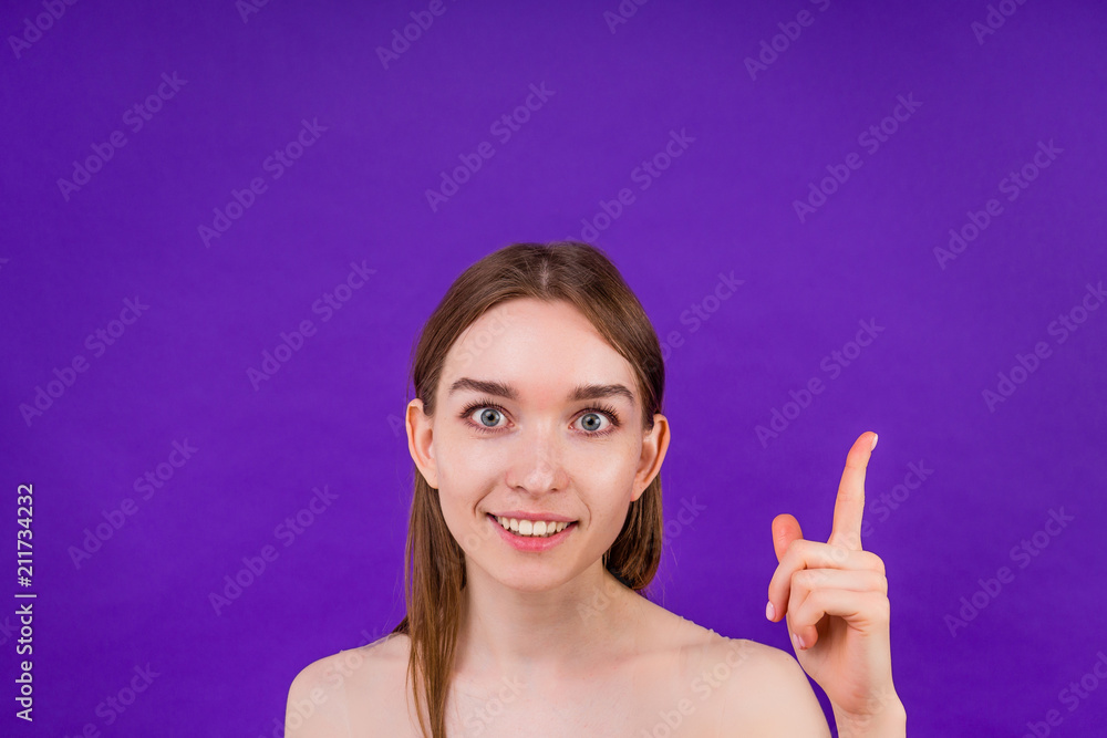 portrait of a beautiful clean woman skin smiling with a toothy smile finger pointing up on a violet background in the studio copyspace portrait of a beautiful clean woman skin smiling with a toothy smile finger pointing up on a violet background in the studio copyspace