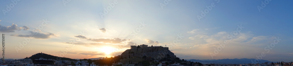 Fototapeta premium Iconic Acropolis hill and the Parthenon as seen from rooftop at sunset with golden colours and beautiful cloud formations, Athens historic center, Attica, Greece