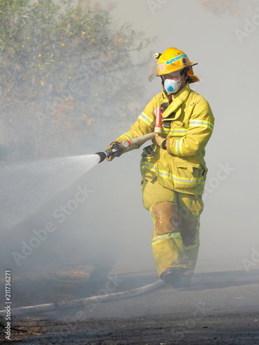 Melbourne, Australia - April 13, 2018: Fire fighter with a hose at a bush fire in an suburban area of Knox City in Melbourne east.