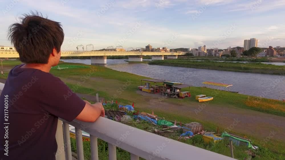 Young JAPANESE MAN looking at the river and thinking of something. At sunset riverside of Tama river in Tokyo. Young JAPANESE MAN looking at the river and thinking of something. At sunset riverside of Tama river in Tokyo.