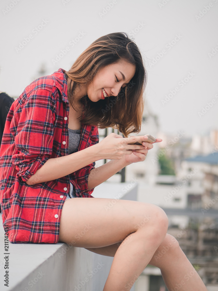 Beautiful young asian woman using smartphone sitting on rooftop in the city. Beautiful young asian woman using smartphone sitting on rooftop in the city.