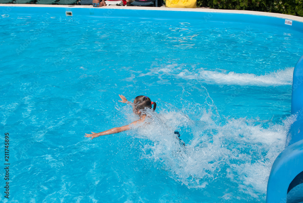 little thin girl in swimming pool with splashes on water slide in summer park