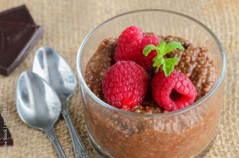 Raw vegan dessert background. Sugar free Carob Chia Pudding with almond milk and raspberries in glass on wooden table. Healthy eating concept. Raw vegan dessert background. Sugar free Carob Chia Pudding with almond milk and raspberries in glass on wooden table. Healthy eating concept.