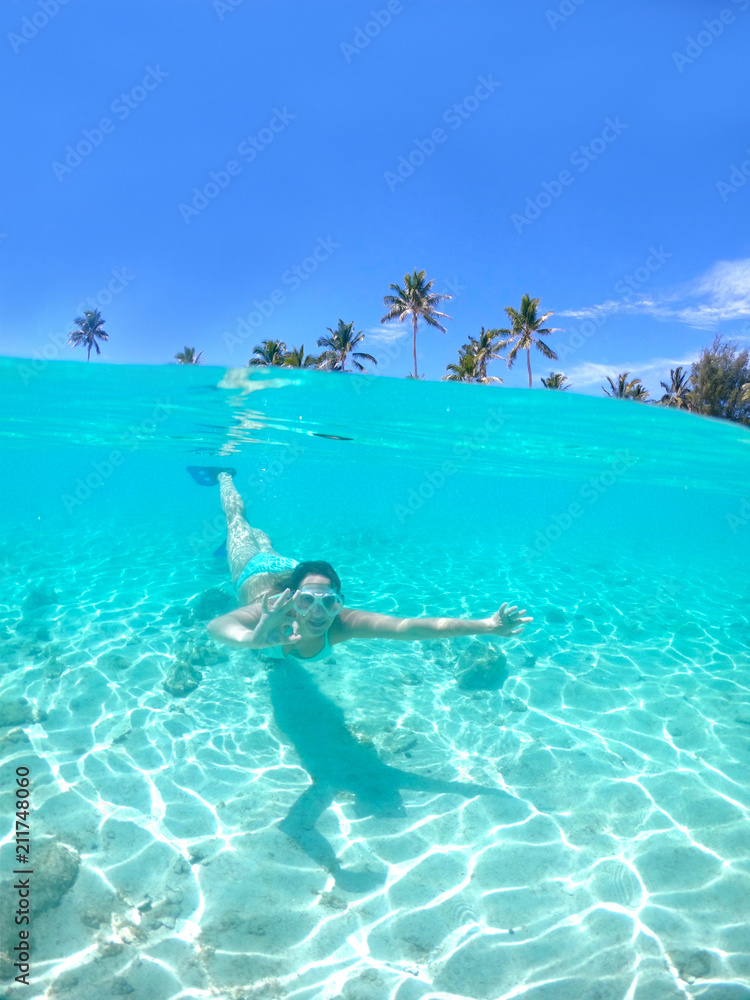 HALF UNDERWATER: Woman snorkels towards the camera and makes the ok gesture.