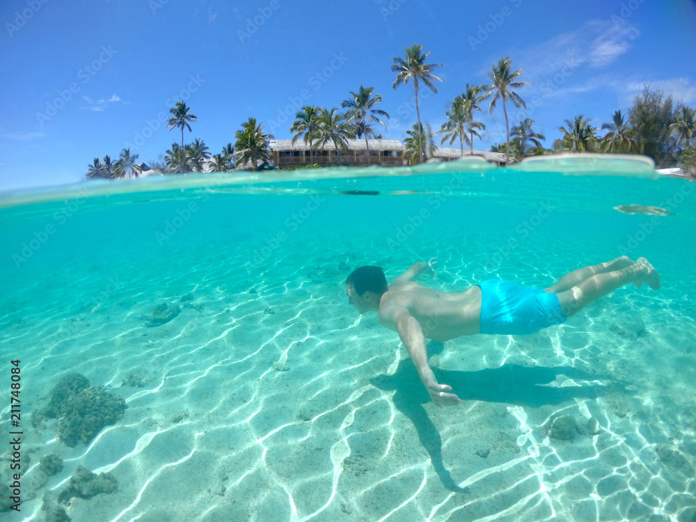 HALF UNDERWATER Active young man swims along the breathtaking exotic sandy shore