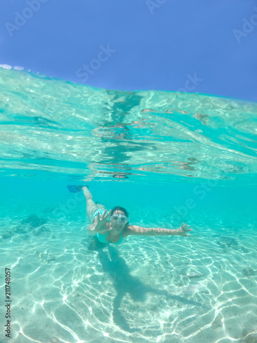 HALF UNDERWATER  Cheerful young woman makes a hand gesture while snorkeling.