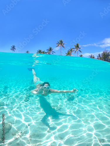 HALF UNDERWATER: Woman snorkels towards the camera and makes the ok gesture.