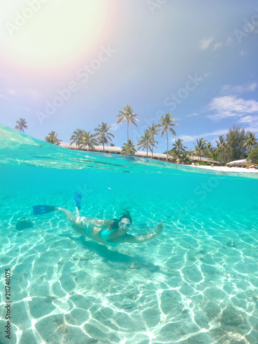 HALF UNDERWATER: Bright sun shines on woman giving the ok sign while snorkeling.