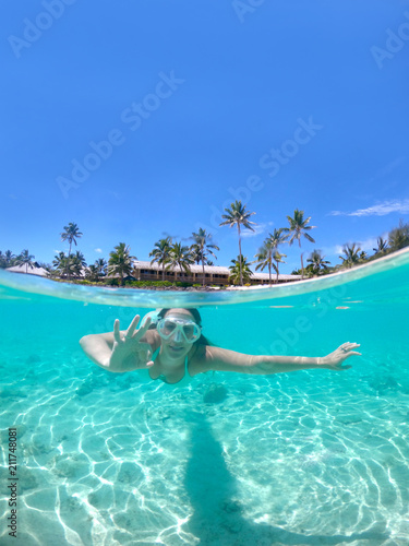 HALF UNDERWATER: Happy girl gives the ok sign while diving in the turquoise sea. © helivideo