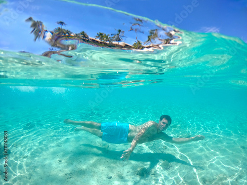 HALF UNDERWATER: Man on vacation swimming underwater in the glassy ocean water.