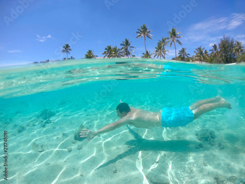 HALF UNDERWATER  man swimming along the white sand beach of tropical island.