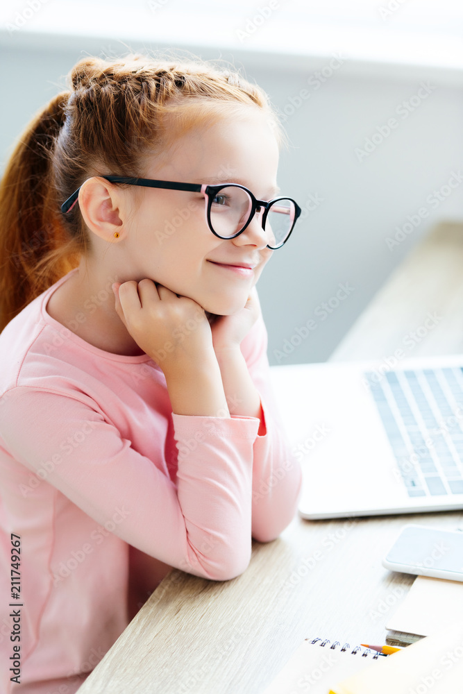 beautiful smiling child in eyeglasses looking away while studying with laptop ay home beautiful smiling child in eyeglasses looking away while studying with laptop ay home