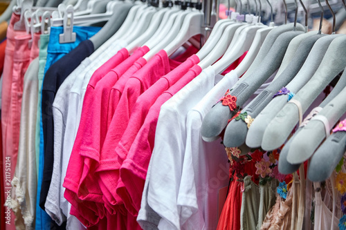Colorful women's summer dresses and t-shirts on hangers in a retail shop. Fashion and shopping concept