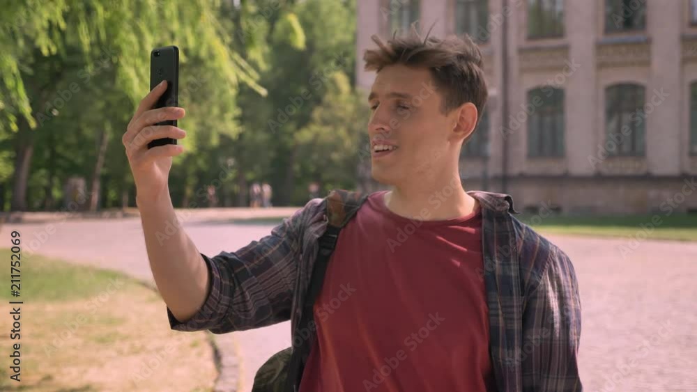 Young handsome man has a videocall in park in daytime in summer, communication concept