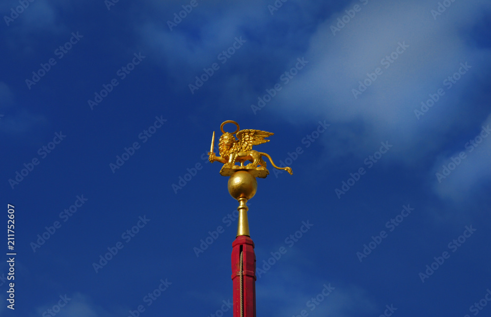 Saint Mark Winged Lion golden statuette wielding a sword against blue sky, a symbol of the Old Venice Republic at war