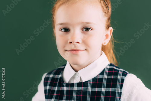 close-up portrait of beautiful little red haired schoolgirl smiling and looking at camera