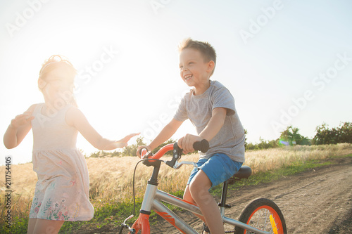  Boy and girl in the field. The boy is riding a bicycle, and the girl is running alongside. A cheerful, happy childhood in the village.