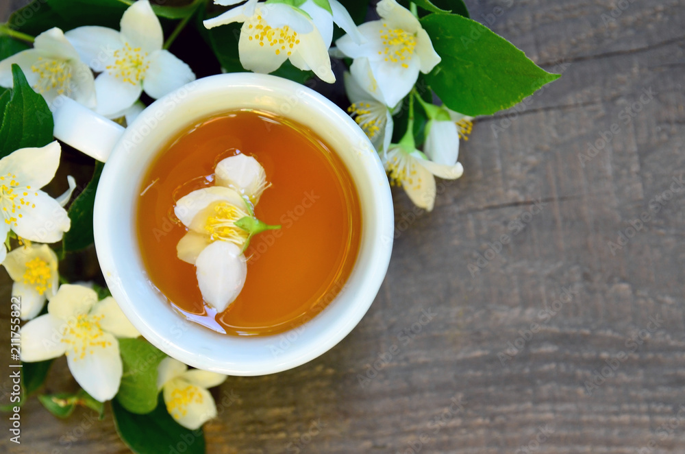 Jasmine tea in a white cup with fresh jasmine flowers on old wooden table.Healthy drink,diet or herbal medicine concept.Top view.Copy space.Selective focus. Jasmine tea in a white cup with fresh jasmine flowers on old wooden table.Healthy drink,diet or herbal medicine concept.Top view.Copy space.Selective focus.