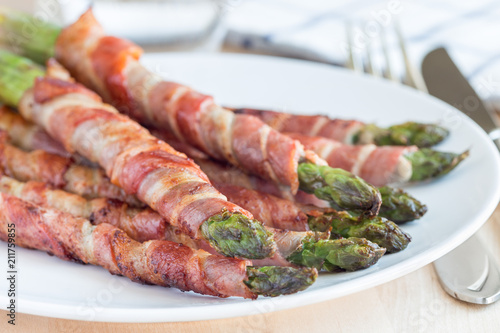 Green asparagus wrapped with bacon on white plate, horizontal