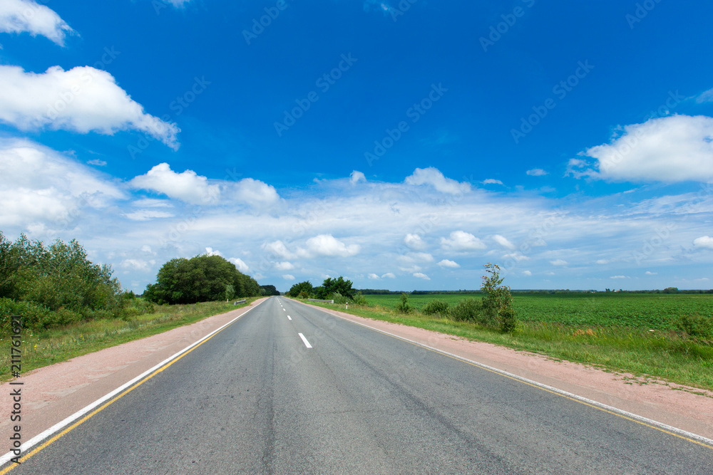 road through the green field and clouds on blue sky in summer day