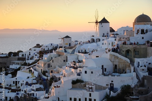 Famous sunset view known as best sunset in the world with white architectures and windmills above the volcanic caldera in the village of Oia in Santorini island, Greece