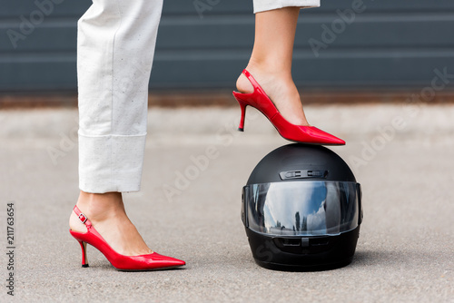 cropped image of woman in red high heels putting leg on motorcycle helmet on street