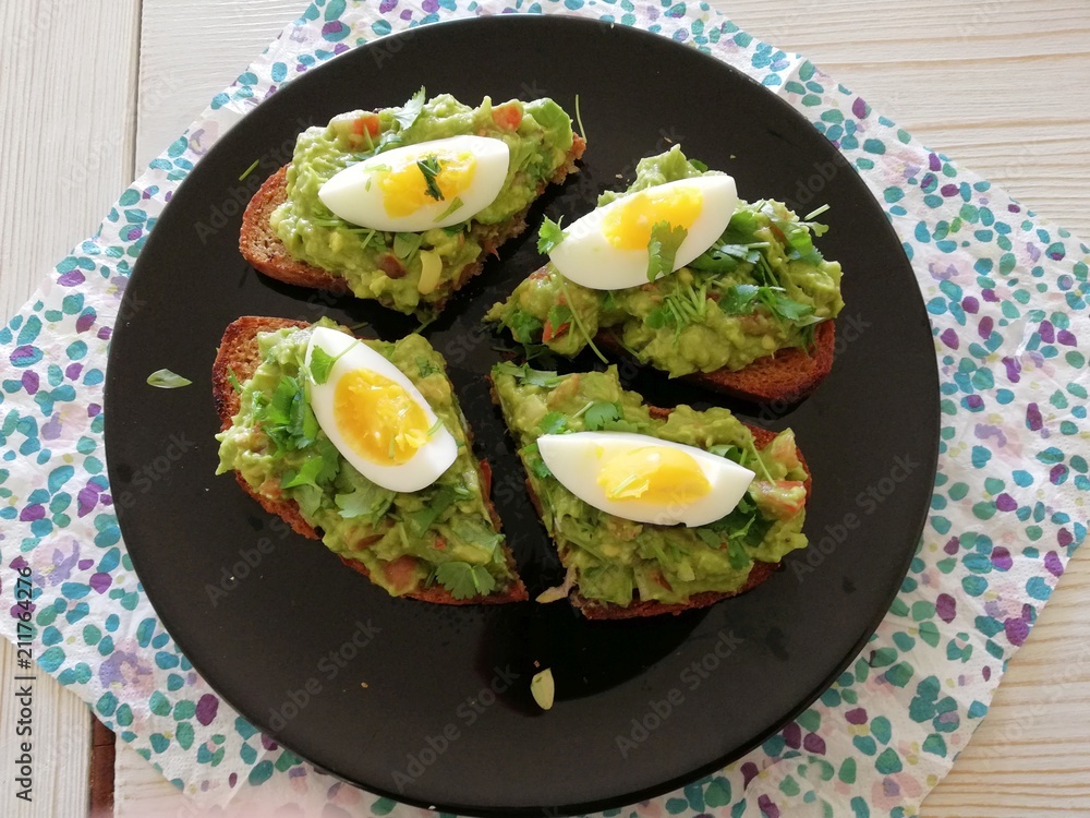 Healthy tasty fresh lunch of homemade guacamole and boiled egg on brown toast served on a black plate Healthy tasty fresh lunch of homemade guacamole and boiled egg on brown toast served on a black plate