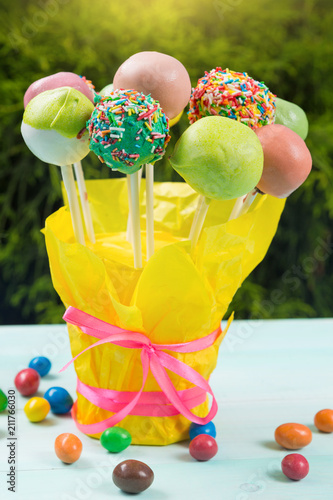 a lot of colored pop cakes in a glass on turquoise boards, in the open air, against a background of greenery scattered around a multicolored candy, selective focusing photo