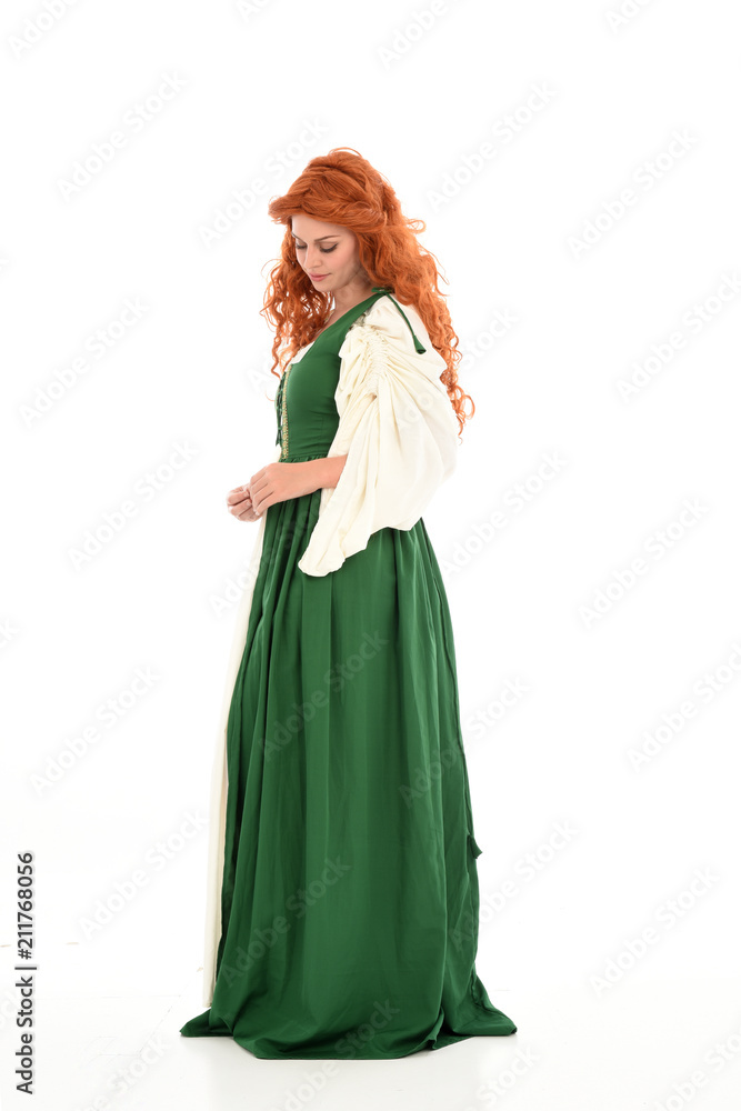 full length portrait of red haired girl wearing long green medieval gown. standing pose, isolated on white studio background.