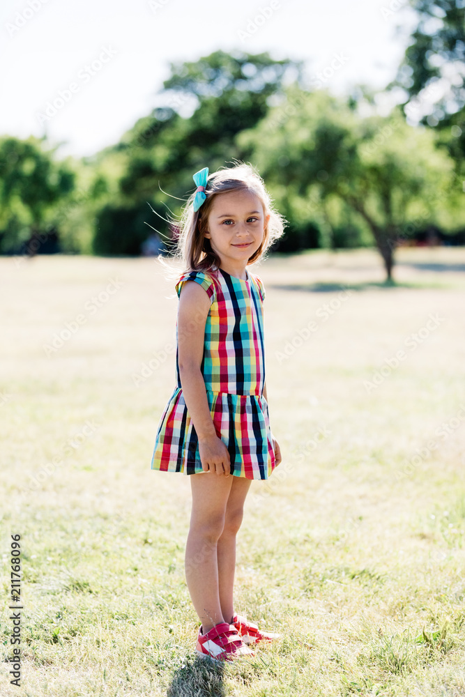 A young happy girl in colorful checkered dress standing in the park, A young happy girl in colorful checkered dress standing in the park,