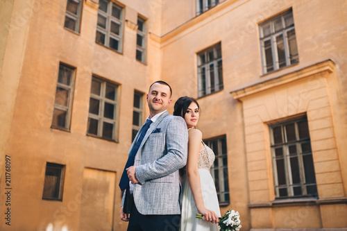 Beautiful newlyweds hug against the background of old buildings with windows. Wedding portrait of loving newlyweds in the old town.
