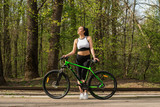 Young woman in a sport bike suit with a bicycle in the park. Health and relaxation.