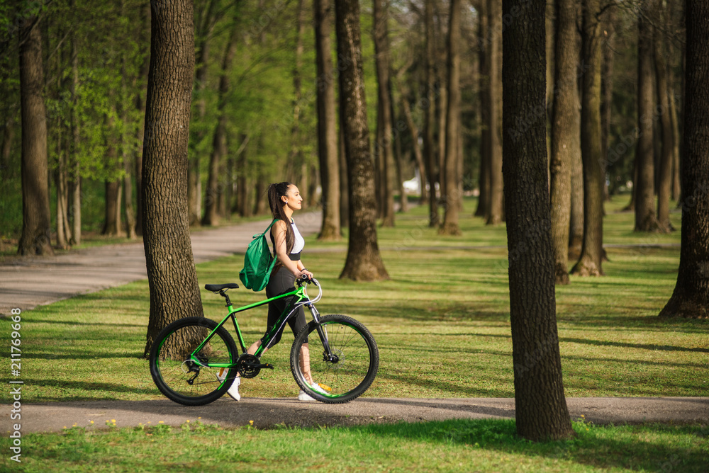 Young woman in a sport bike suit with a bicycle in the park. Health and relaxation.