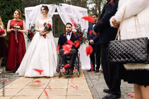 Bride, groom on the wheelchair and their friends stand before an altar during the ceremony