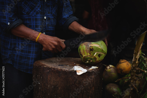 A man is cutting a fresh young green coconut with a sharp chopper or aruval for tourists