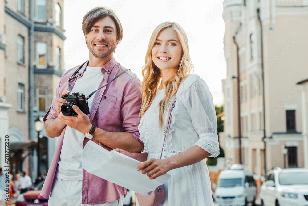 portrait of smiling tourists with map and photo camera on city street