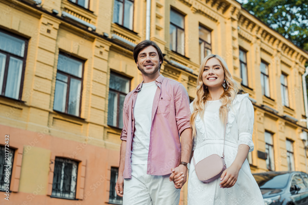 young couple holding hands while walking on city street together young couple holding hands while walking on city street together