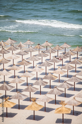 Aerial shot of many straw umbrellas on a beach by the sea.