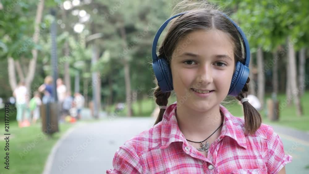 Portrait of cute girl with blue headphones skating in the park. Slow motion footage Portrait of cute girl with blue headphones skating in the park. Slow motion footage