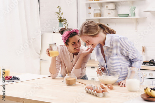 Two cheerful friends cook together desserts and gossip in the kitchen