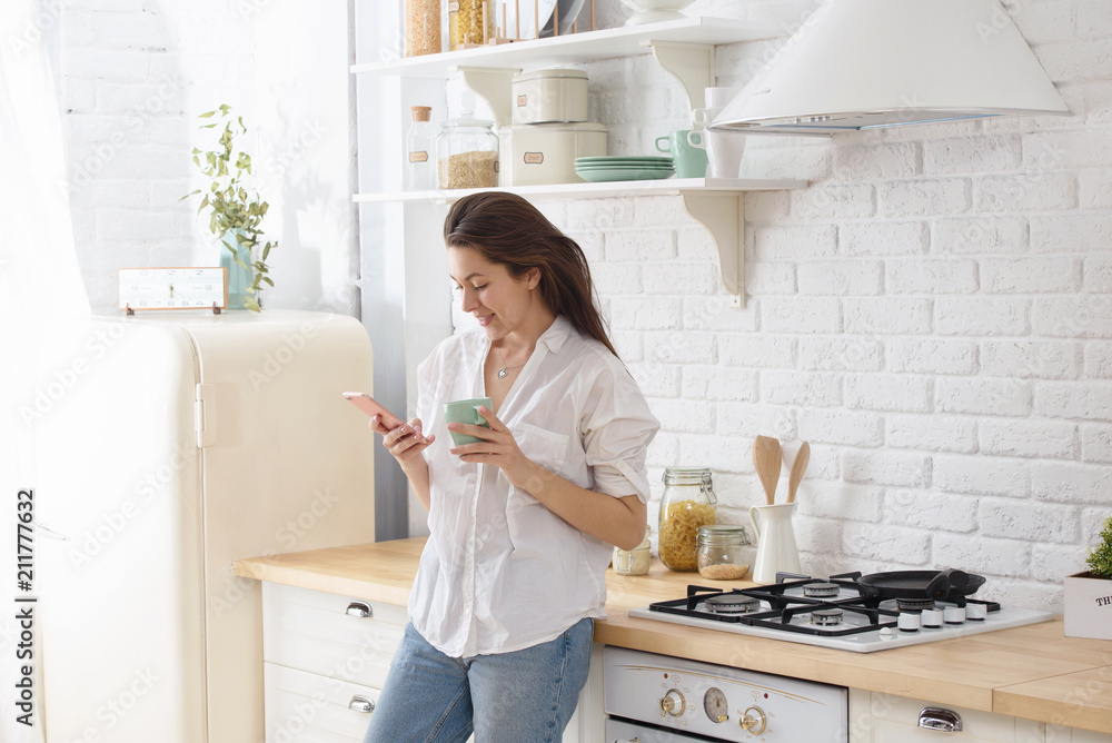 Young beautiful woman in the kitchen, drinking coffee and talking on the phone. Young beautiful woman in the kitchen, drinking coffee and talking on the phone.
