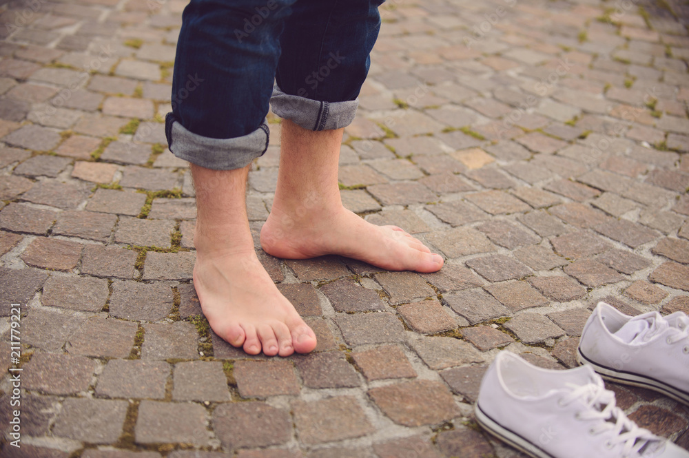 barefooted man standing in street at his white gumshoes