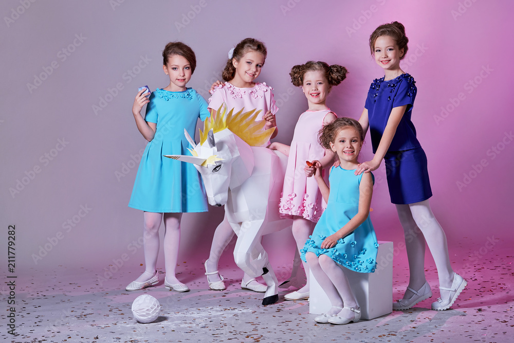 Group little girl in beautiful pink,blue dresses next with unicorn figure.  Five lady children together,clothes,catalog fashion collection.Cheerful  girlfriends,studio,pastel background.Models 5 kids. Stock Photo