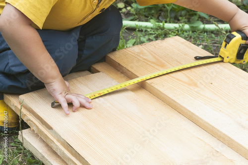 A child measures a wooden board with a tape measure